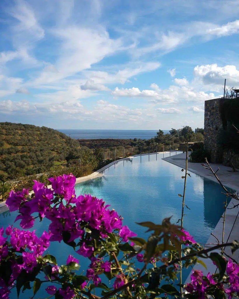 Historic stone-built luxury hotel nestled in Greek hillside, featuring arched windows and terraces overlooking Mediterranean landscape