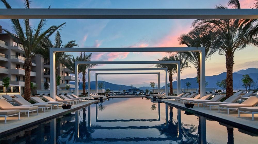 Elegant waterfront luxury hotel with Venetian-inspired architecture, surrounded by palm trees and mega yachts in Porto Montenegro marina