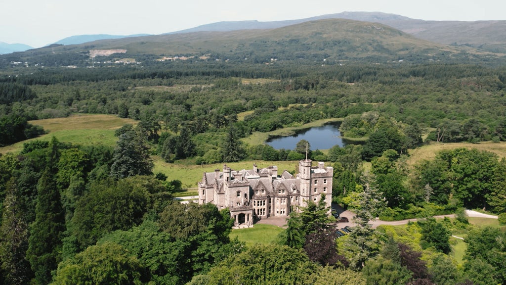 Majestic stone castle hotel with turrets nestled among lush gardens, reflecting in a serene lake with Scottish Highlands in background