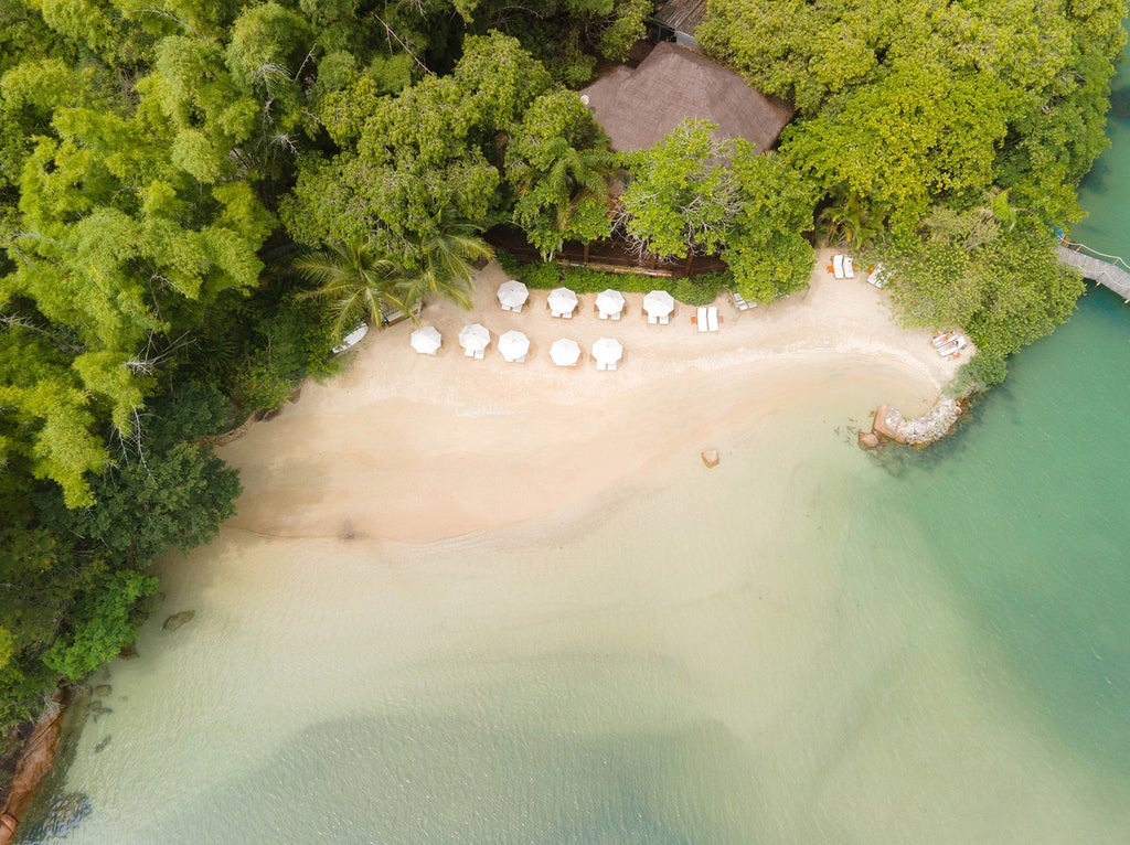 Luxurious overwater bungalow with wooden deck extending into turquoise bay, surrounded by lush Brazilian coastline at sunset