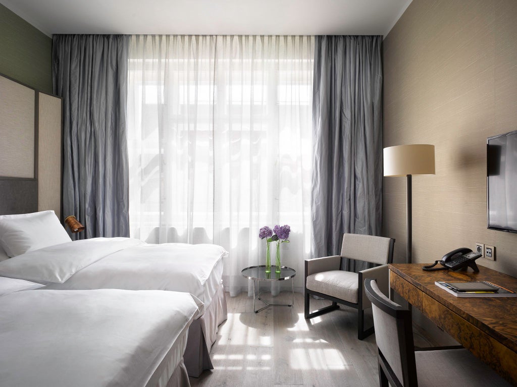 Elegant twin bedroom with contemporary design, plush white linens, dark wood furnishings, and city view at luxurious scenset hotel in Prague's historic center