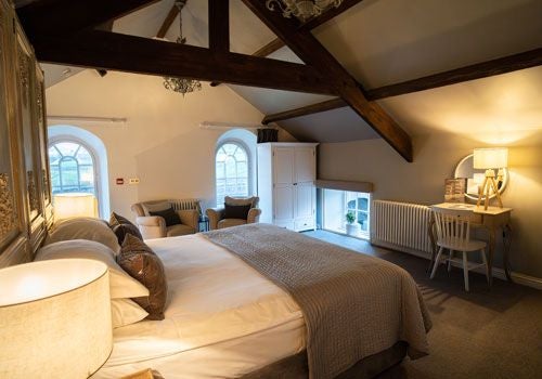 Luxurious bedroom at scenic boutique hotel, featuring elegant white linens, exposed wooden beams, and soft natural lighting with countryside views.