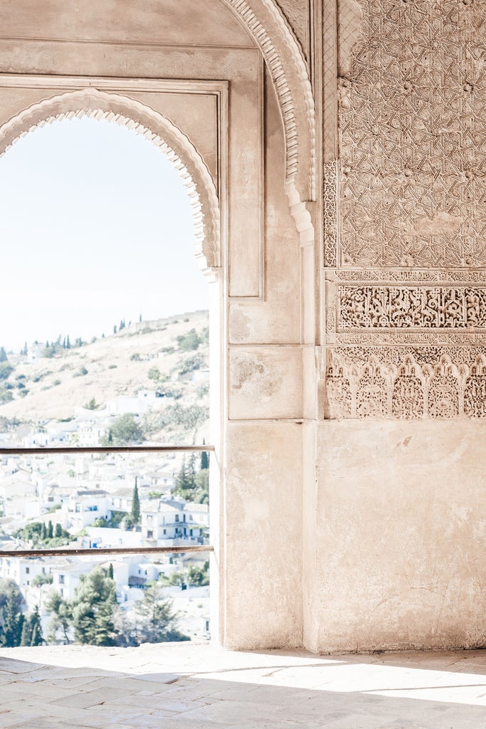 Sunset view of Alhambra palace in Granada, with ornate Islamic architecture perched on hilltop against golden sky and Sierra Nevada mountains