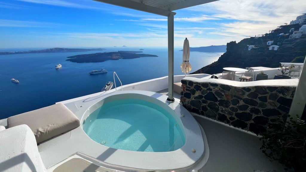 Whitewashed cave suite with panoramic Aegean Sea view, minimalist design, private terrace, and blue-domed architecture of scenic Santorini landscape