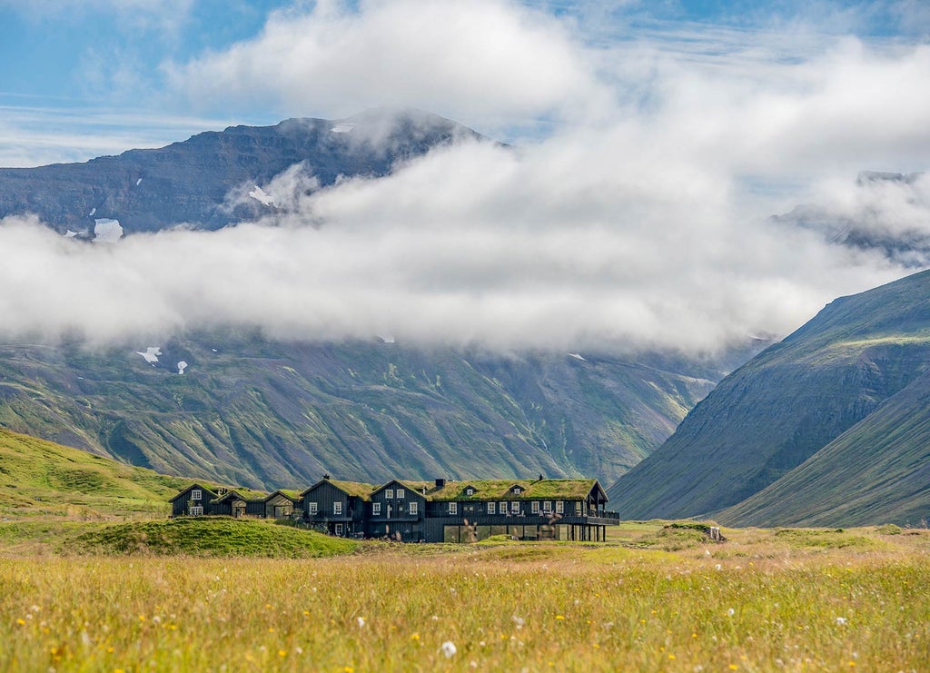 Modern Nordic hotel with black wood exterior and panoramic windows nestled in snow-covered valley beneath dramatic mountains