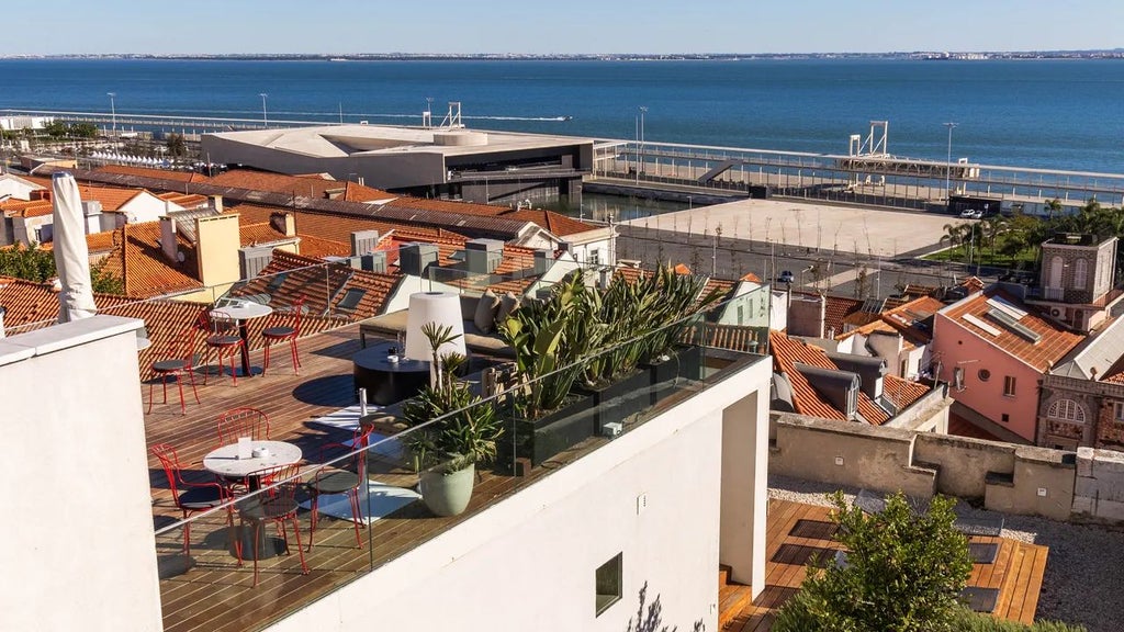 Boutique hotel terrace overlooking Lisbon's historic Alfama district with vibrant tiled rooftops, elegant minimalist design, and panoramic sunset views