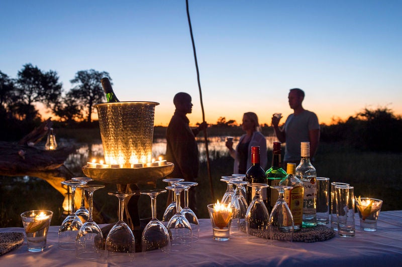 Elevated safari lodge on wooden stilts overlooking Okavango Delta wetlands, with thatched roof and private viewing deck at sunset