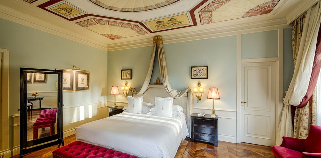 Opulent deluxe hotel room with ornate gold-framed mirror, crystal chandelier, antique furniture and plush king bed with silk drapes