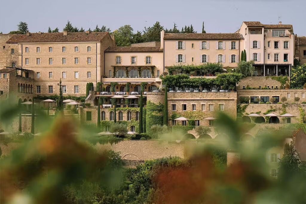 Historic stone luxury hotel La Bastide de Gordes perched on cliff edge with terraced gardens overlooking Provençal valley at sunset