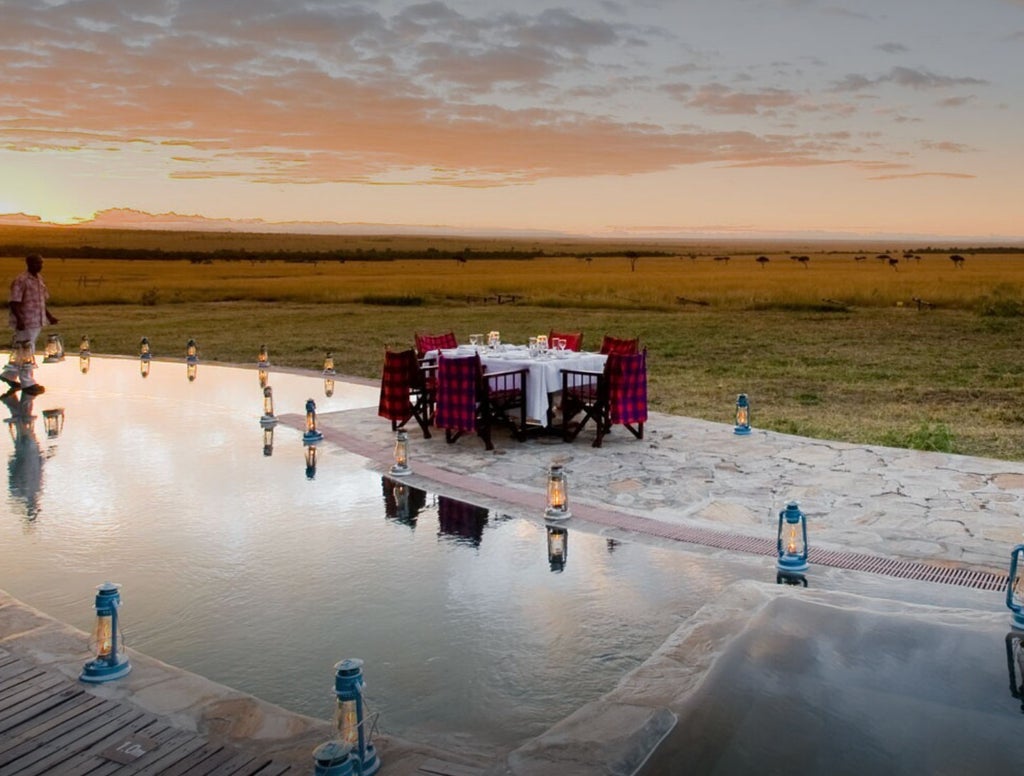 Luxurious safari tent overlooking Masai Mara savanna at sunset, with elegant outdoor deck and traditional thatched roof