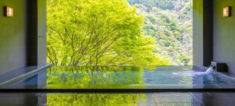 Traditional Japanese onsen ryokan perched on steep mountainside with private cable car, outdoor hot spring baths overlooking misty valley