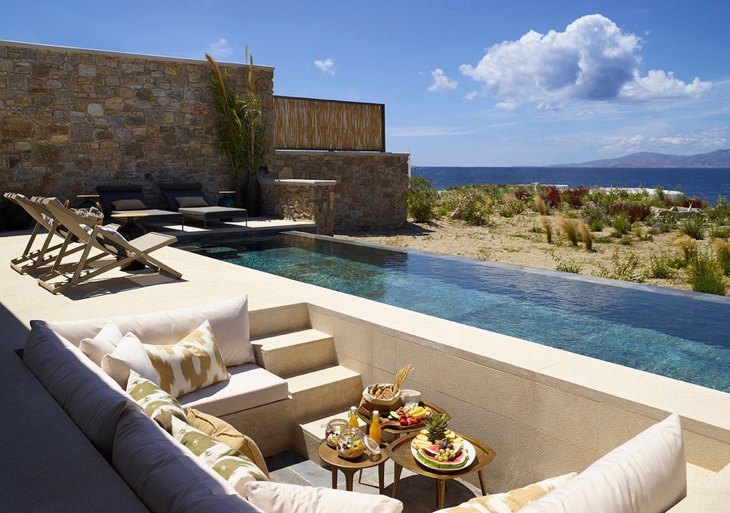 Luxurious one-bedroom villa with private heated pool overlooking azure Aegean Sea, featuring modern minimalist design and stunning Mykonos landscape backdrop