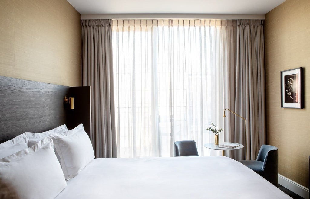 Elegant junior suite with plush white bedding, modern minimalist decor, soft ambient lighting, and luxurious textures in a chic boutique hotel room setting