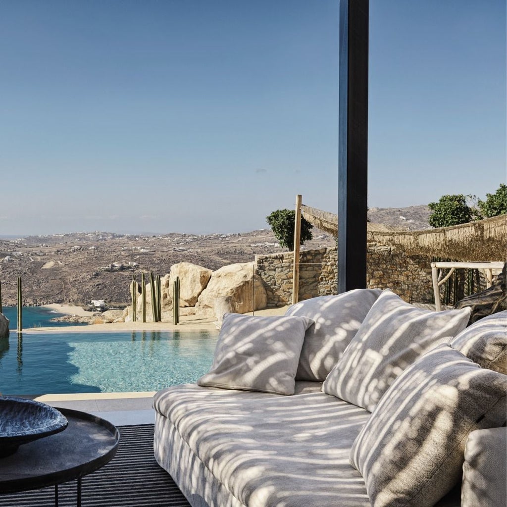 Luxurious infinity pool overlooking Aegean Sea at sunset, white minimalist architecture cascading down Mykonos hillside