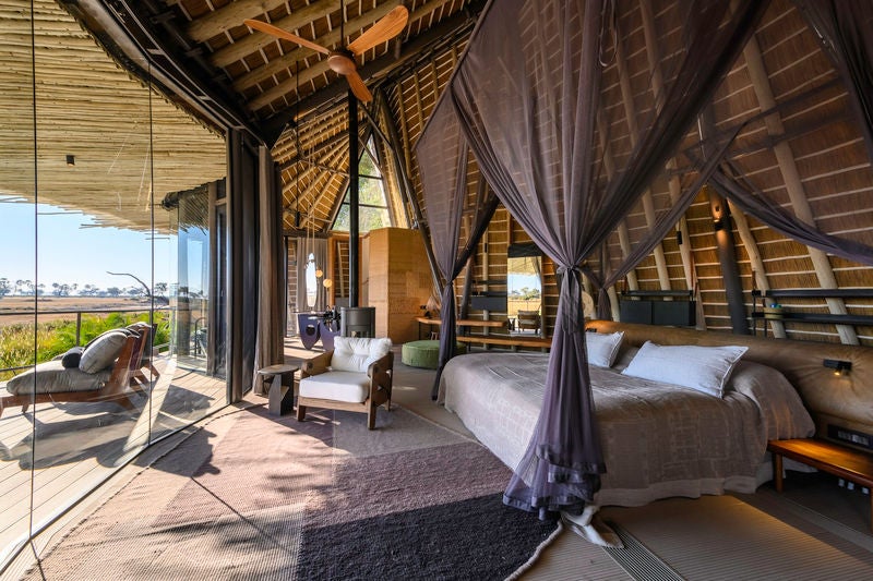 Elevated wooden luxury safari lodge with wrap-around deck overlooking pristine Okavango Delta wetlands at sunset golden hour