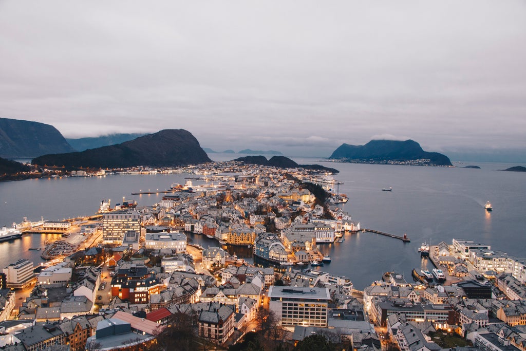 Coastal city of Ålesund with Art Nouveau architecture stretches across islands, surrounded by fjords and snow-capped mountains at sunset