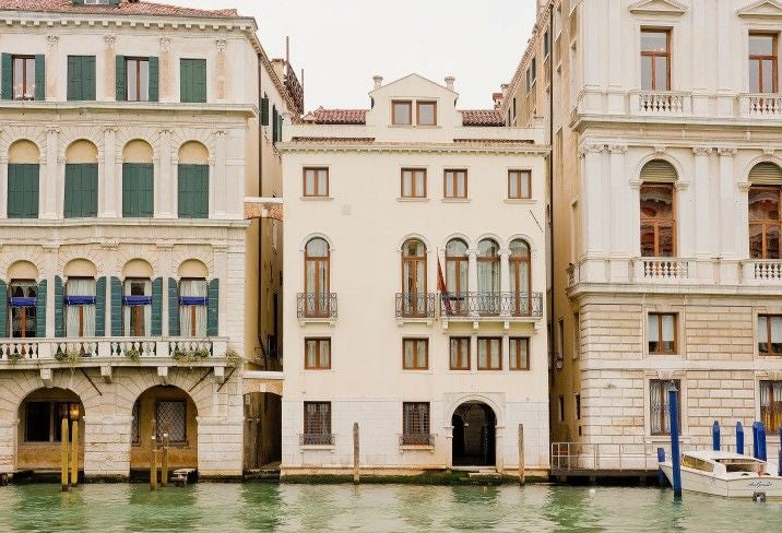 Elegant waterfront Venetian hotel with ornate Gothic architecture, marble columns and arched windows reflecting in Grand Canal at sunset