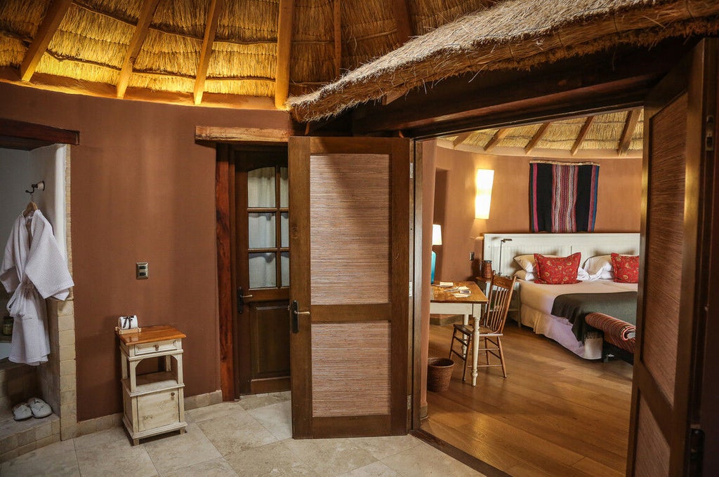 Upscale desert lodge featuring rustic adobe walls, traditional thatched roof, and elegant outdoor seating under wooden pergolas at dusk