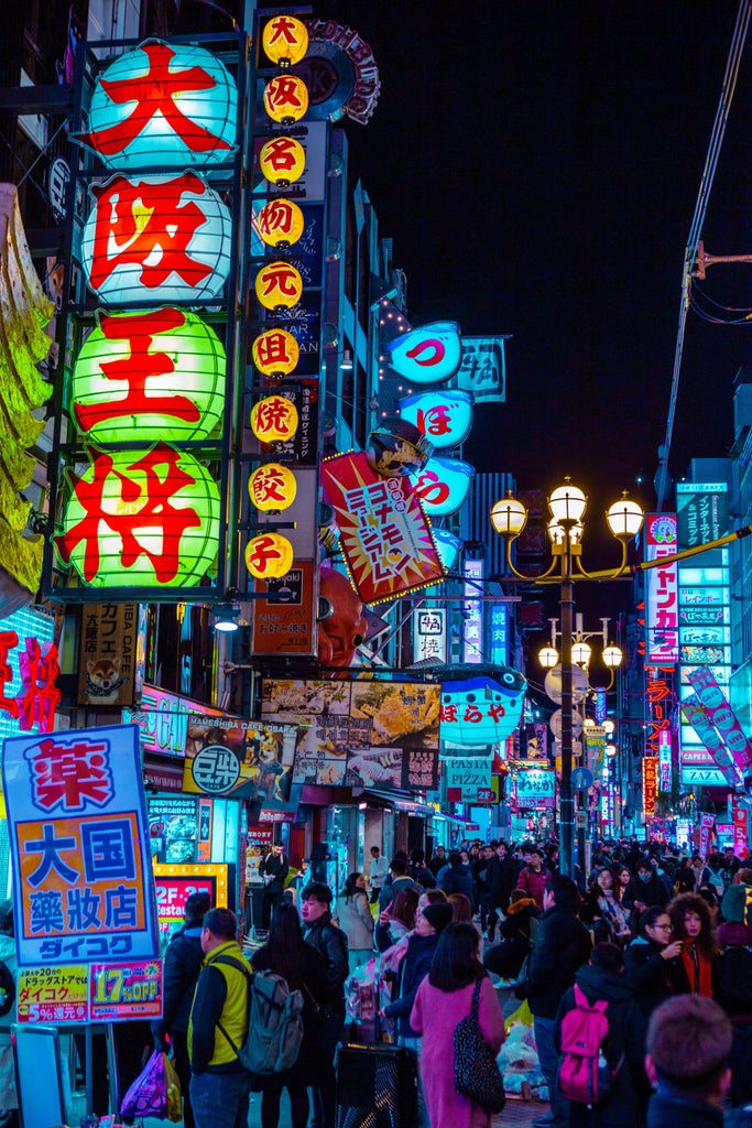 Aerial view of Osaka at night, illuminated skyscrapers and neon lights reflect in Dotonbori River, iconic landmarks glow in cityscape