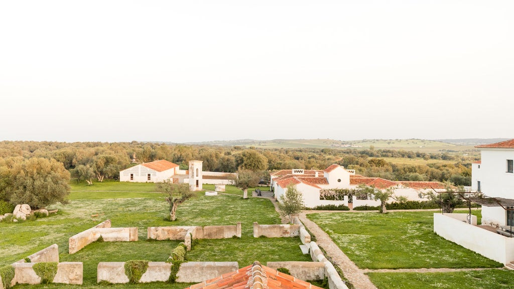 Elegant stone-walled luxury hotel in rural Portugal with white facade, terracotta roof tiles and manicured gardens under blue skies