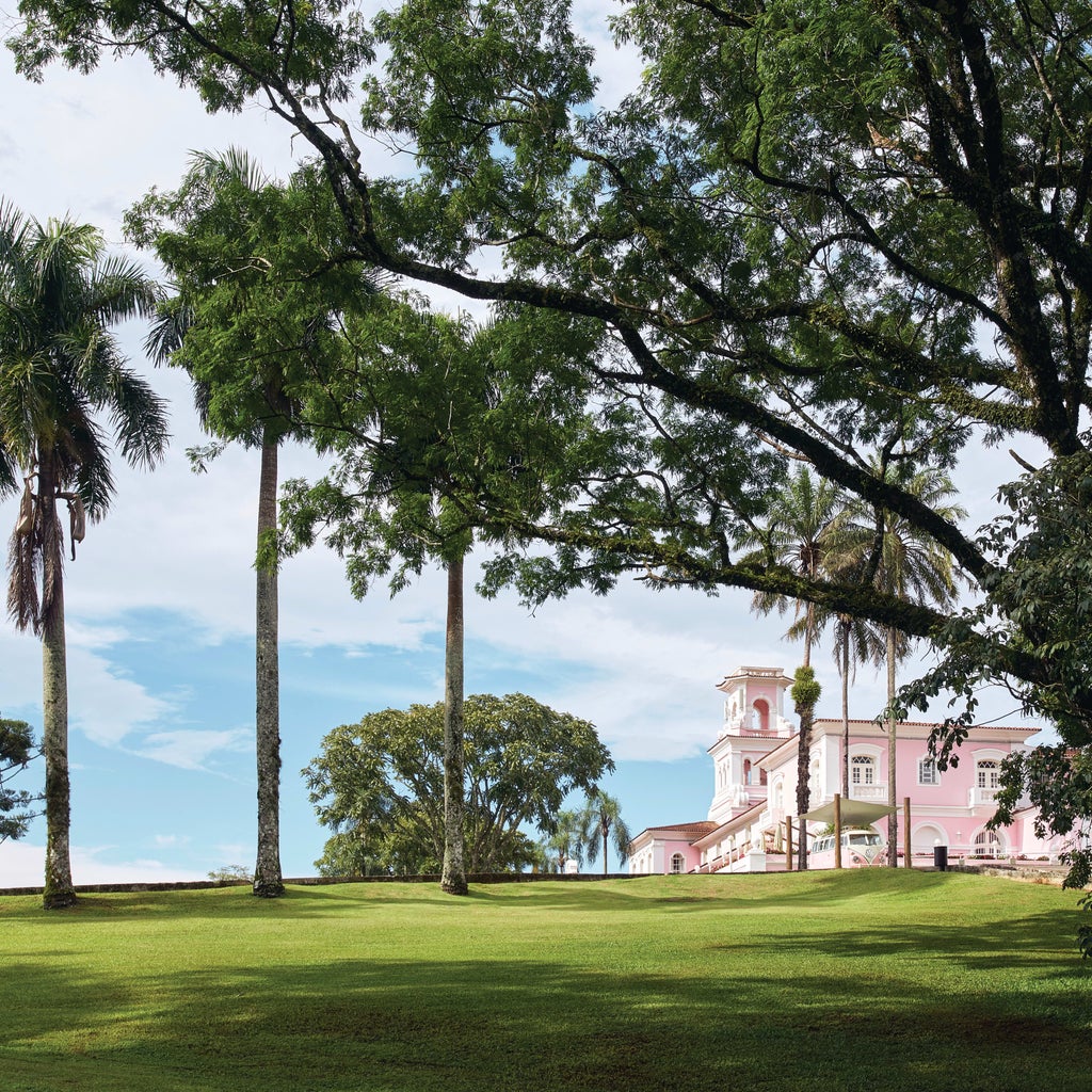 Pink-hued colonial luxury hotel nestled in lush rainforest, featuring grand archways, manicured gardens, and palm-lined pathways