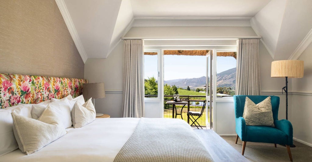 Luxurious merlot-colored hotel room with plush king bed, elegant furnishings, and large windows overlooking South African vineyard landscape at Mont Rochelle wine estate