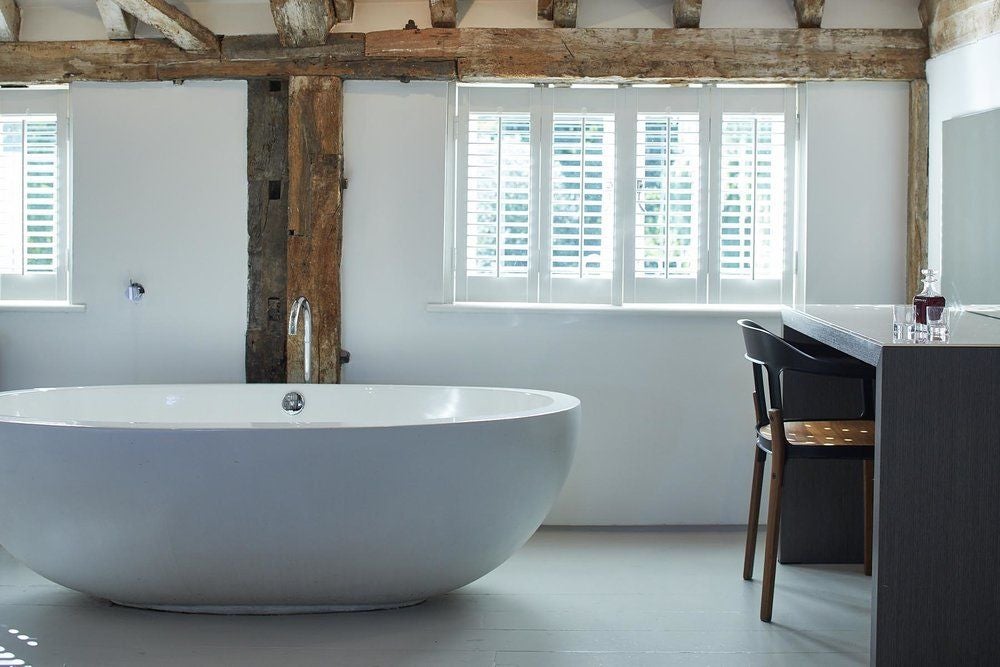 Luxurious hotel room with soft neutral tones, exposed wooden beams, crisp white bedding, and vintage mill-inspired architectural details at Tuddenham Mill