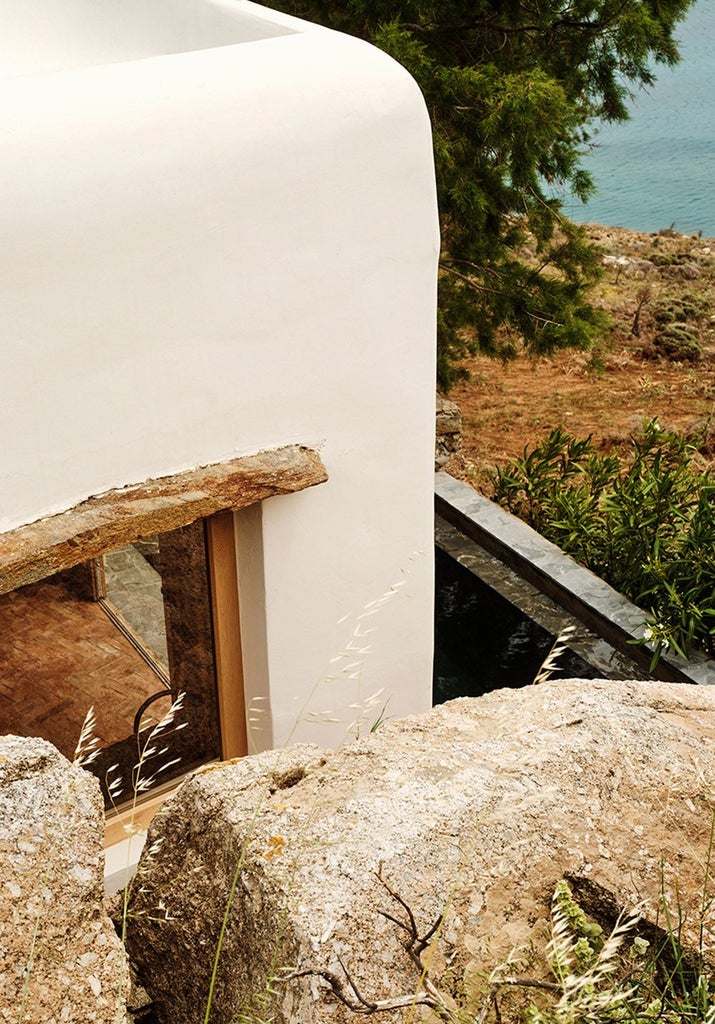 Luxurious minimalist white hotel overlooking azure Aegean waters with sleek architectural design and infinity pool against dramatic Greek island landscape