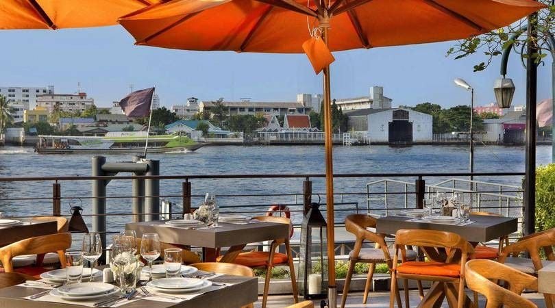 Luxurious riverside hotel in Bangkok with colonial-style architecture, featuring a waterfront infinity pool and elegant wooden terraces