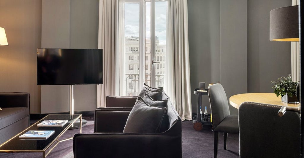 Elegant suite with expansive city views, plush king bed, contemporary Spanish design, marble bathroom, and luxurious Gran Vía ambiance in downtown Madrid hotel