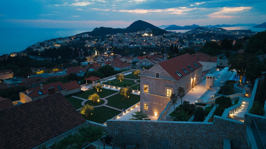 Elegant beachfront hotel with white stone facade, palm-lined promenade, and private balconies overlooking the turquoise Adriatic Sea