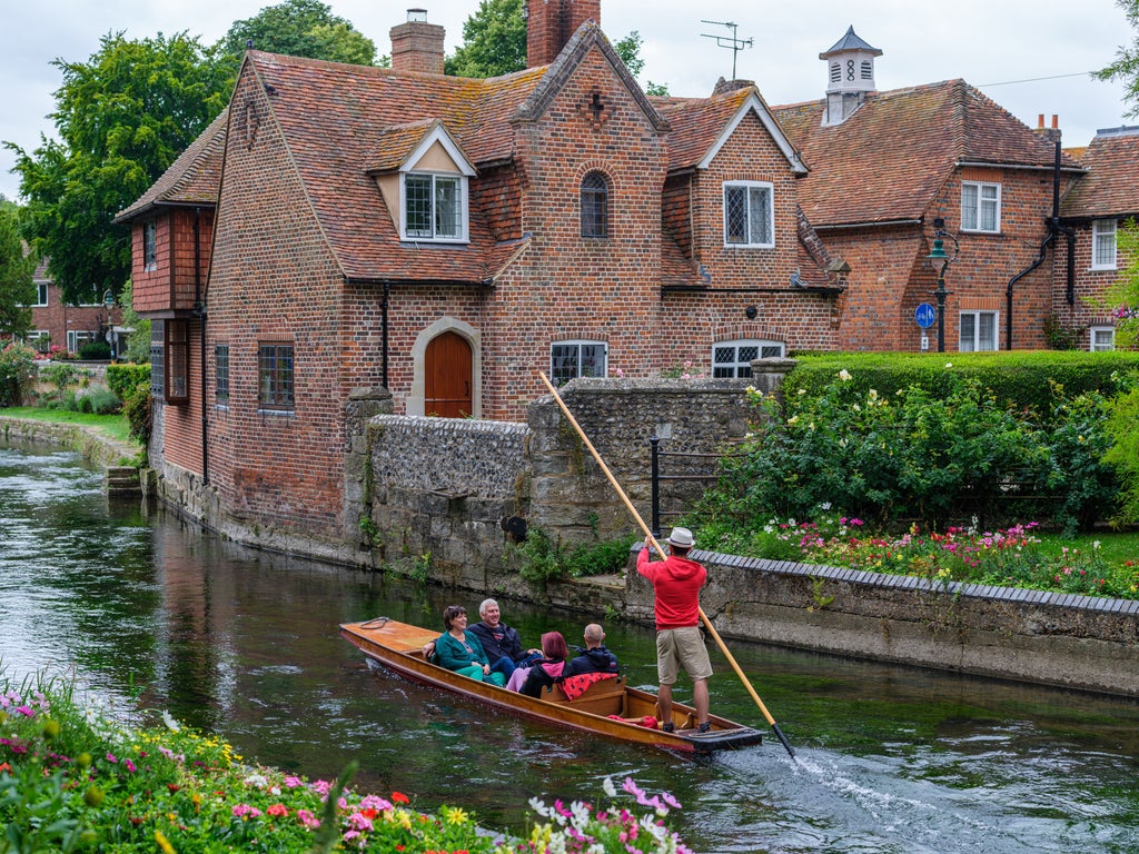 Historic Canterbury Cathedral towers rise above medieval city streets, with timber-framed shops and cobblestone walkways in afternoon light