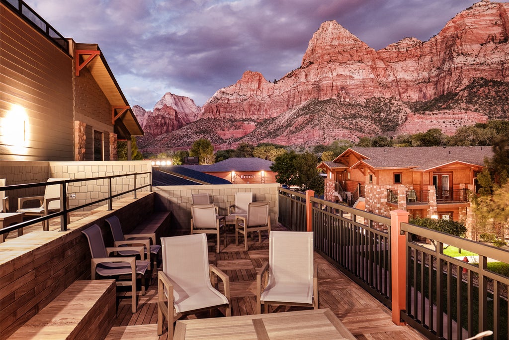 Upscale mountain lodge nestled against red cliffs, featuring modern stone architecture, glass balconies, and landscaped desert gardens