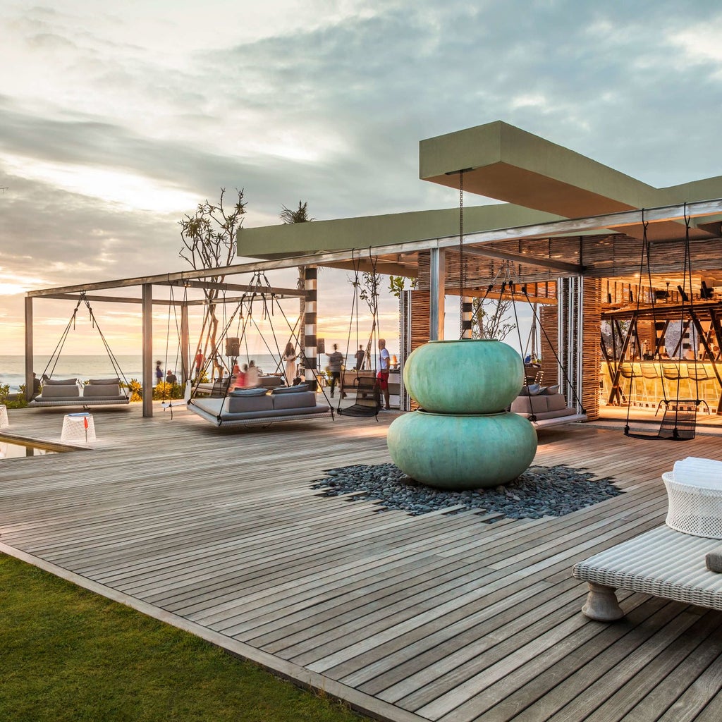 Modern, L-shaped infinity pool overlooking Canggu beach, surrounded by sleek white loungers and swaying palm trees at sunset