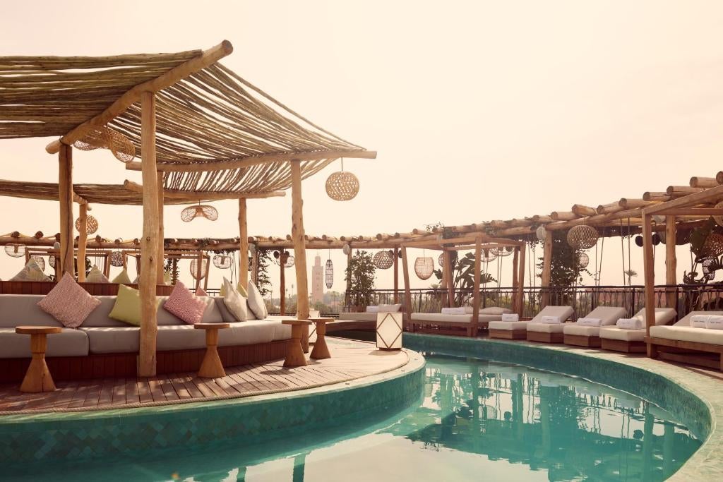 Modern luxury hotel facade with traditional Moroccan archways, sleek white walls, and palm trees set against a vibrant sunset sky in Marrakech