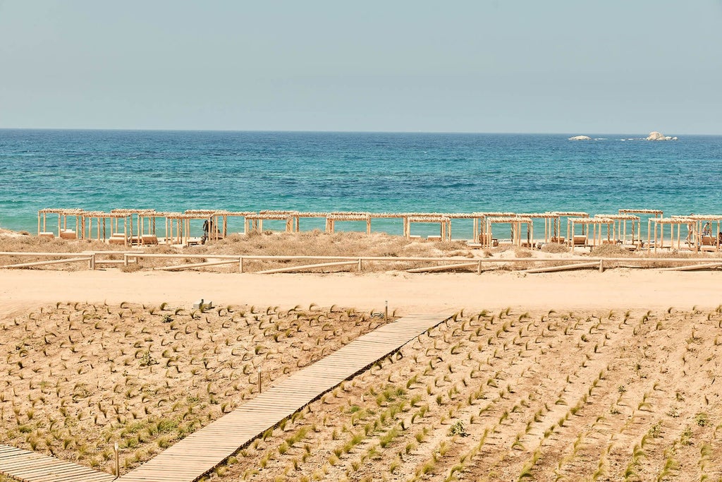 Luxurious beachfront hotel with white-washed Cycladic architecture, crystal-clear azure waters, and pristine sandy shoreline in scenic Greek island setting