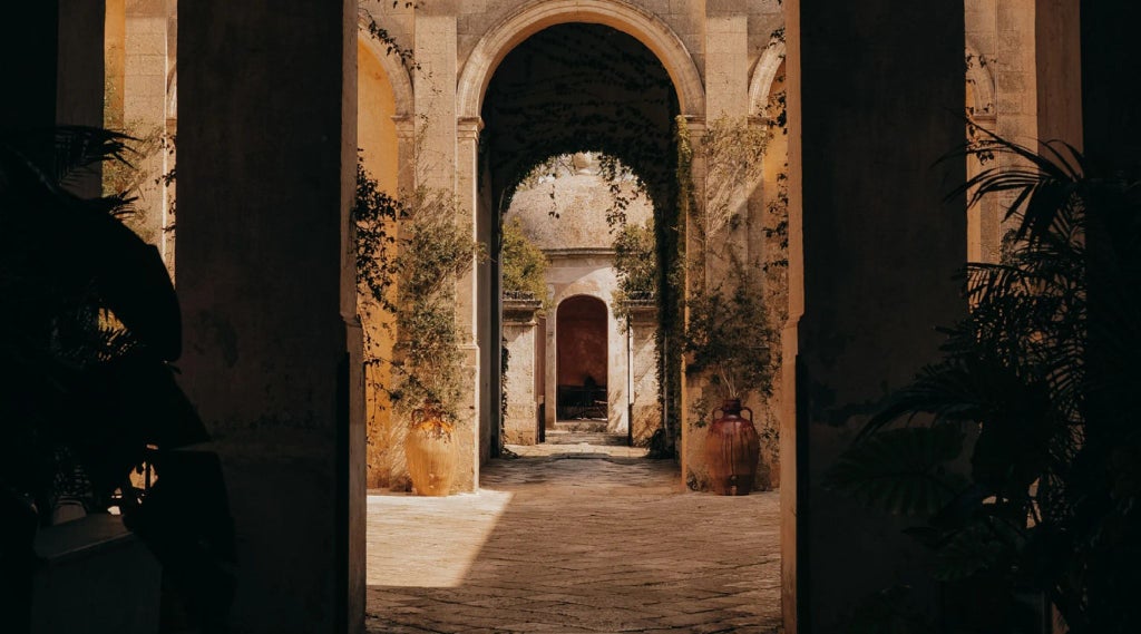 A luxurious pale stone villa with elegant architecture, ornate balconies, and arched windows, set against the golden light of an Italian afternoon in Puglia