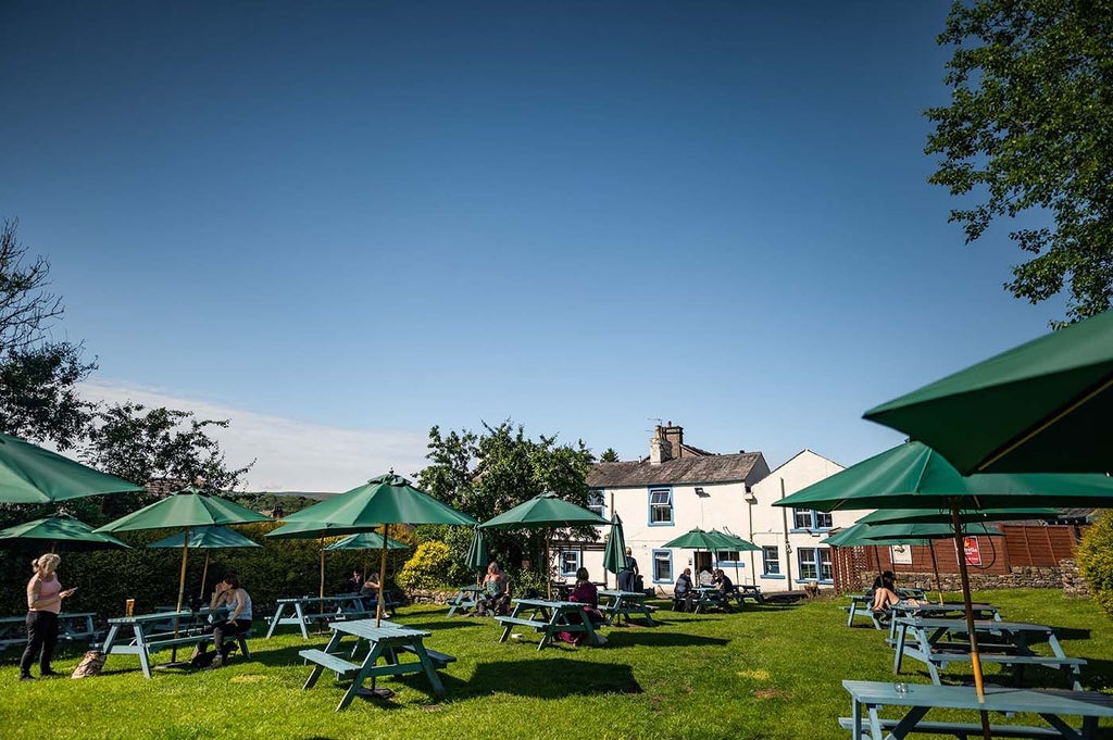 Charming stone-built countryside inn with rustic wooden signage, nestled in lush green landscape, exuding traditional British hospitality and pastoral elegance