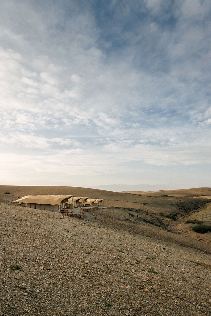 Luxurious desert camp with white canvas tents nestled among rolling Moroccan sand dunes at sunset, featuring modern glamping amenities