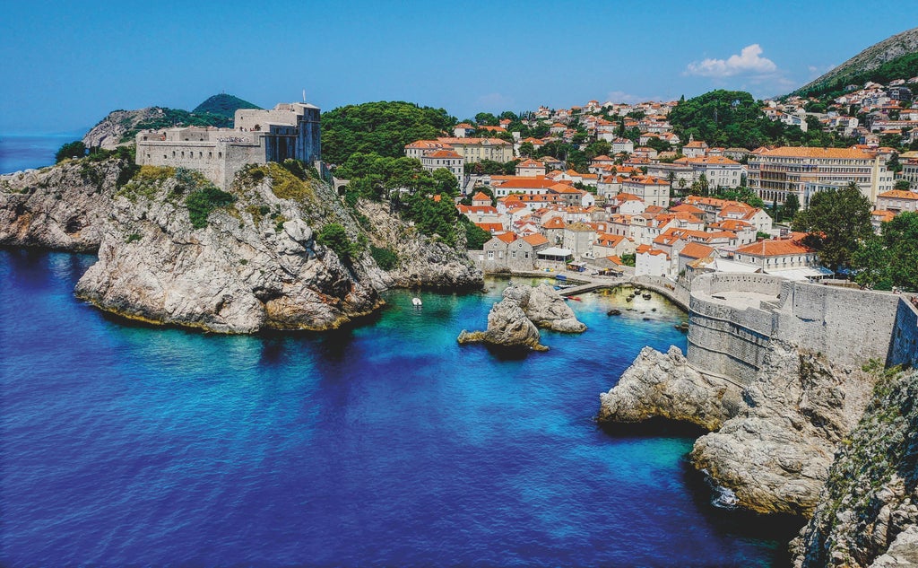 Historic stone walls of Dubrovnik rise above the Adriatic Sea, terracotta rooftops and limestone streets glow in warm sunset light