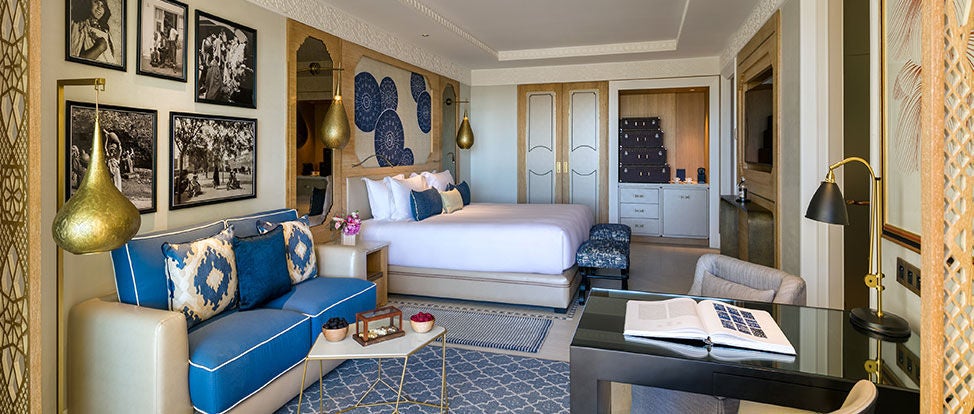 Elegant hotel room with forest views featuring a king bed, modern Moroccan decor, arched windows, and plush seating in warm earth tones