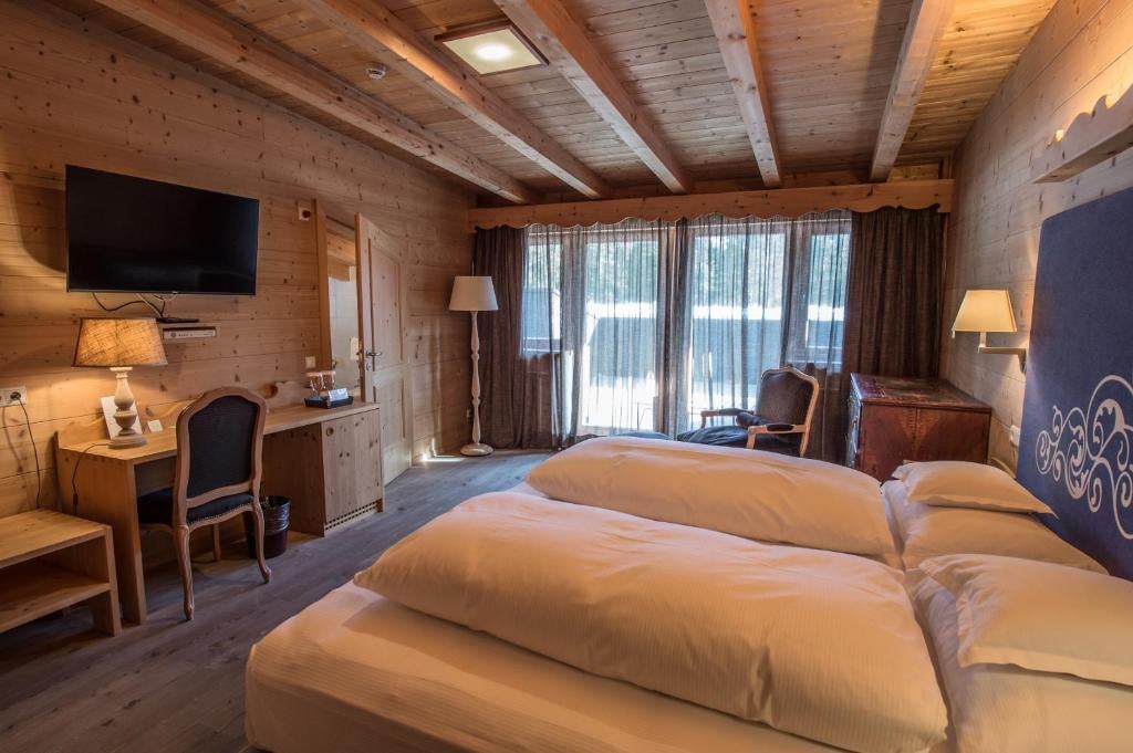 Luxurious alpine junior suite featuring wood-paneled walls, king bed with crisp linens, cozy seating area, and mountain-view balcony