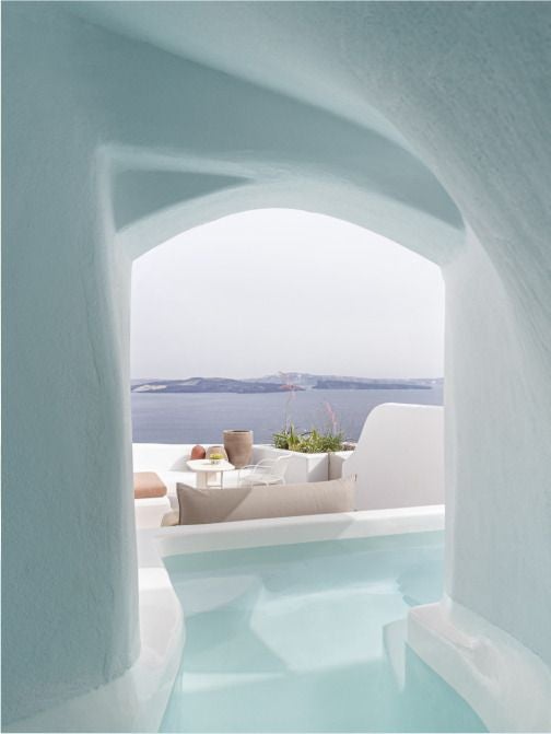 Luxurious white Cycladic hotel with blue-domed architecture overlooking azure Aegean Sea, elegant infinity pool against Santorini's dramatic volcanic landscape