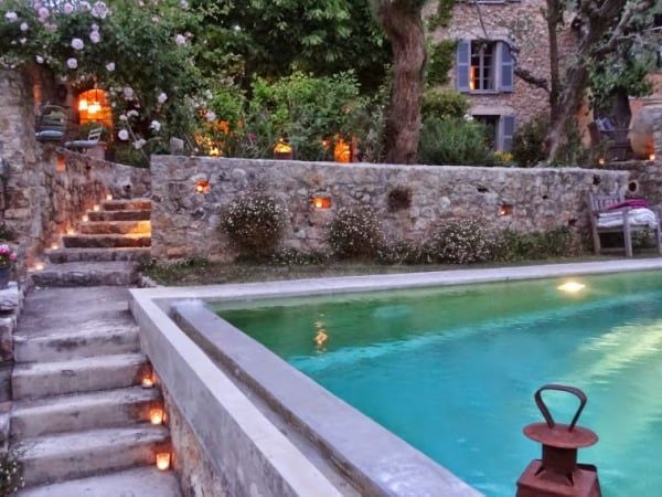 Elegant French countryside hotel with soft pink rose-adorned exterior, manicured lavender gardens, and traditional stone architecture bathed in golden sunlight