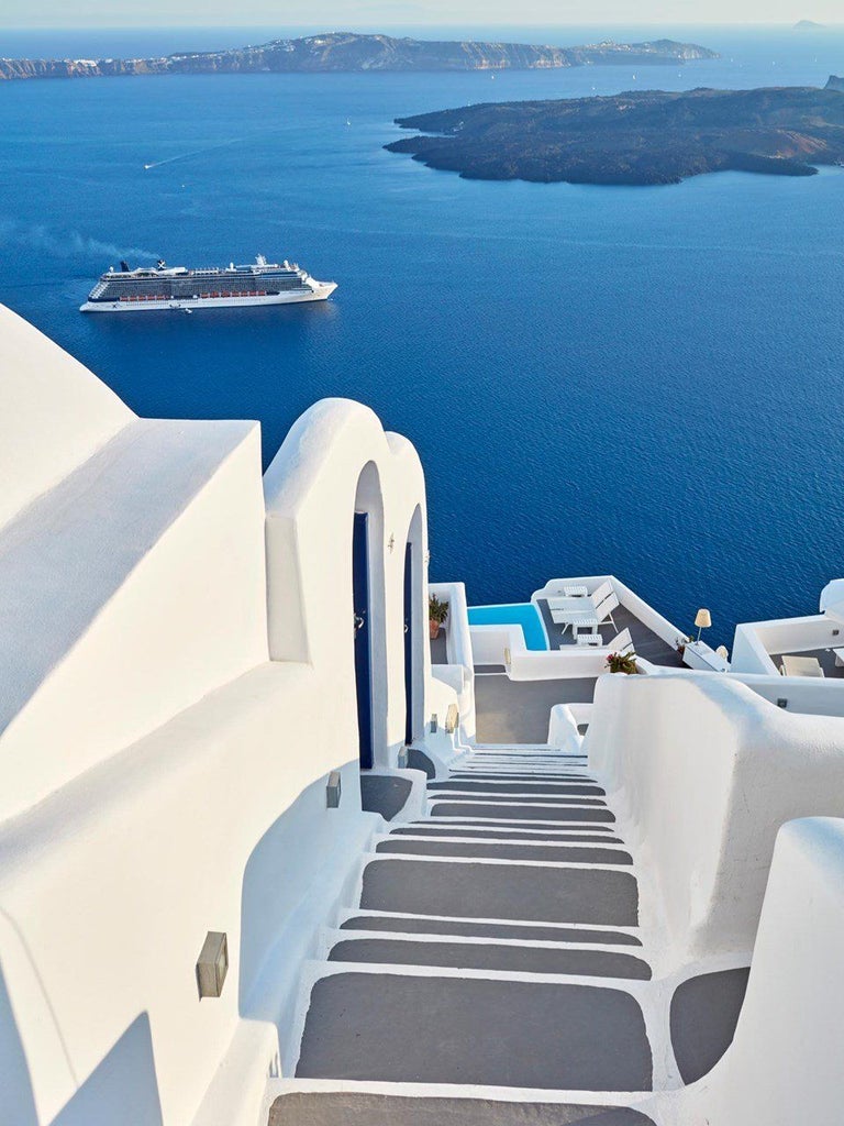 Whitewashed luxury hotel with infinity pools cascading down Santorini's dramatic cliffside, overlooking the azure Aegean Sea at sunset