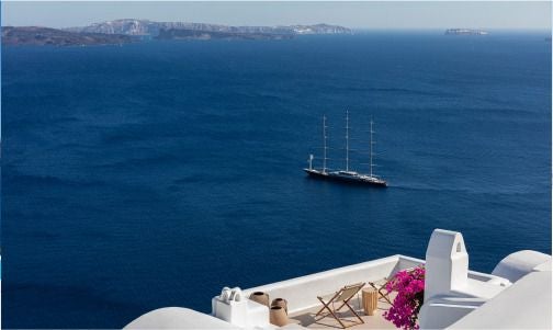 Luxurious white-washed Cycladic hotel perched on Oia's cliff, featuring infinity pool with stunning blue Aegean Sea panorama at sunset