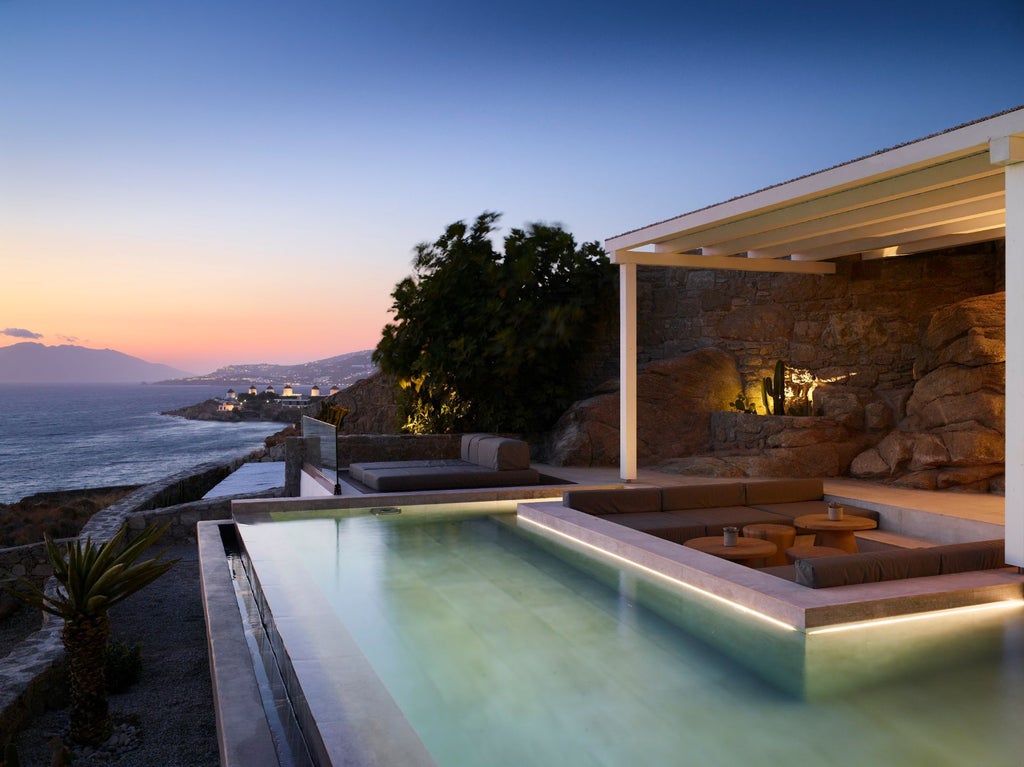 Elegant infinity pool overlooking the Aegean Sea at dusk, with minimalist white loungers and atmospheric lighting at luxury Greek resort