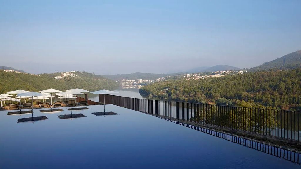 Luxurious infinity pool overlooking Portugal's Douro Valley vineyards, with modern sunbeds and panoramic river views at sunset