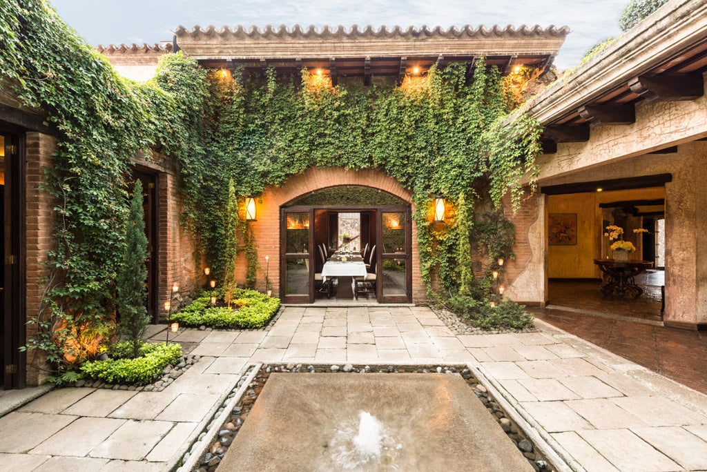 Elegant colonial-style boutique hotel with stone archways, wrought iron details, and lush courtyard gardens illuminated by warm lighting