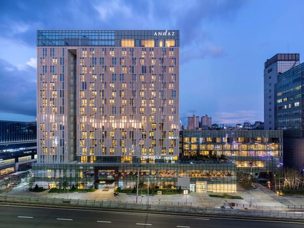 Modern luxury hotel Andaz Seoul facade with sleek glass exterior reflecting cityscape, geometric patterns and warm lighting at dusk